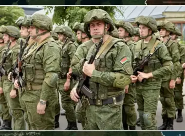 Belarusian soldiers in green uniforms and helmets stand in formation carrying rifles.