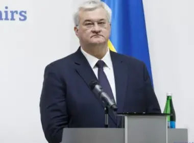 Ukrainian Foreign Minister Andrii Sybiha stands behind a lectern with a microphone and a Ukrainian flag in the background.