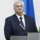 Ukrainian Foreign Minister Andrii Sybiha stands behind a lectern with a microphone and a Ukrainian flag in the background.