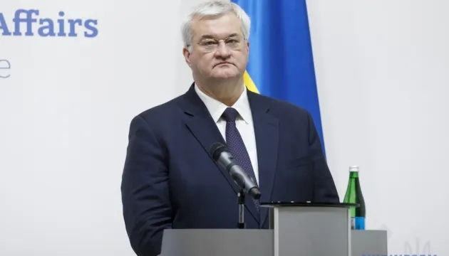 Ukrainian Foreign Minister Andrii Sybiha stands behind a lectern with a microphone and a Ukrainian flag in the background.